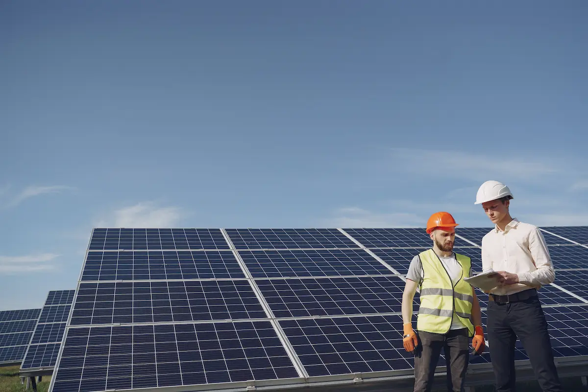 Jeune professionnel casqué et technicien en gilet consultent un document devant des panneaux solaires